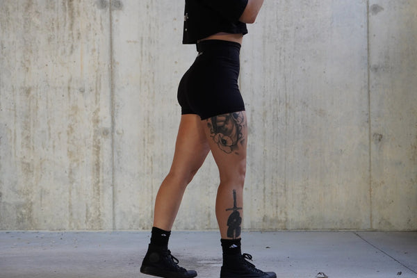 Girl wearing black shorts and shoes with a concrete wall background