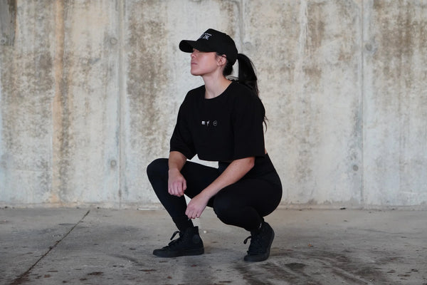 Person in black outfit squatting against a textured wall