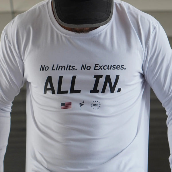 White long-sleeve shirt with motivational text 'No Limits. No Excuses. ALL IN.' on a blurred background