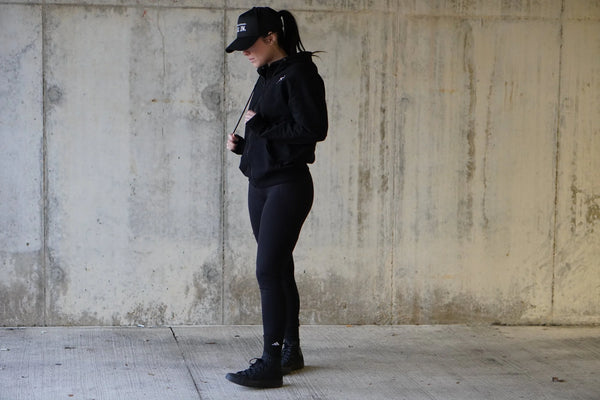 Woman wearing a black outfit standing against a textured wall.