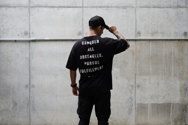 Person wearing a black t-shirt with motivational text against a concrete wall