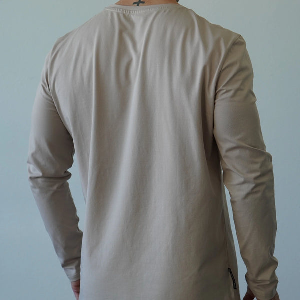 Person wearing a beige long-sleeve shirt against a plain background