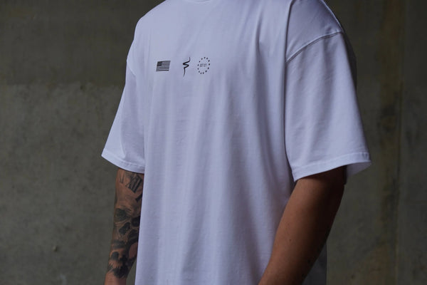 White t-shirt with No Straight Path® logos on the front, worn by a person with tattoos, against a neutral background.