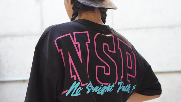 Woman wearing a black t-shirt with a pink and blue No Straight Path® logo on the back.