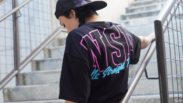 Woman wearing a black t-shirt with a colorful No Straight Path® logo, standing on stairs.