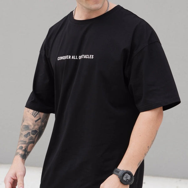 Person wearing a black t-shirt with 'CONQUER ALL OBSTACLES' text on a gray background