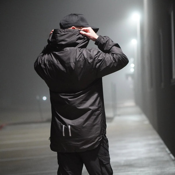 Person wearing a black jacket and cap in a foggy urban setting