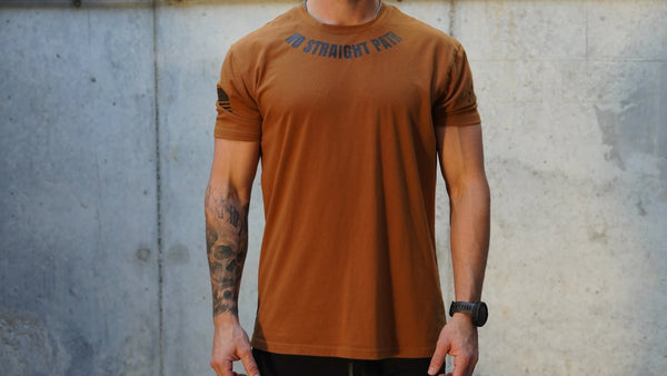 Person wearing a brown t-shirt with No Straight Path® text against a concrete wall.