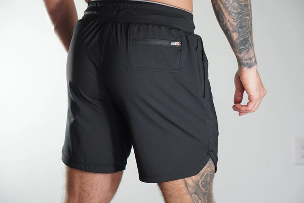 Person wearing black shorts with a pocket on a plain background