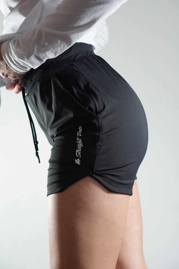 Person wearing black athletic shorts with a No Straight Path® logo on a plain background