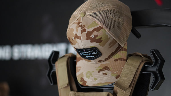 Camouflage baseball cap with a No Straight Path® patch on a dark background