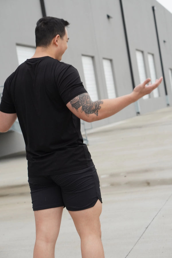 Man in black t-shirt and shorts standing outdoors with arms outstretched