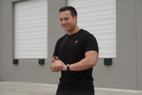 Man wearing a black t-shirt with a white No Straight Path® logo, standing indoors with gray walls and windows.