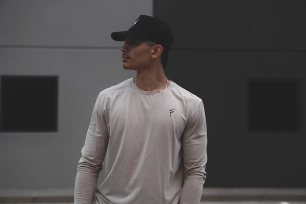 Man wearing a beige long-sleeve shirt with a No Straight Path® logo on a blurred background.