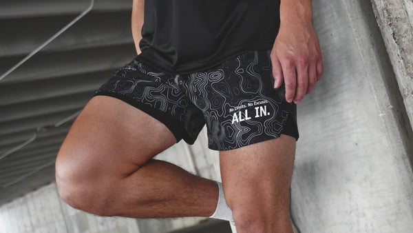 Person wearing black shorts with white text and design, standing on a concrete surface.