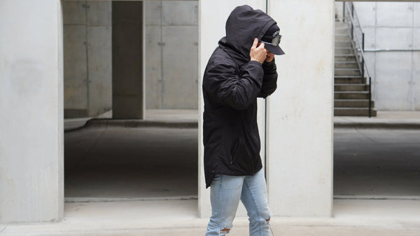 Person wearing a black jacket and jeans standing in an urban setting.