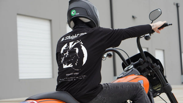 Person wearing a black tee with a white graphic on a Harley motorcycle.