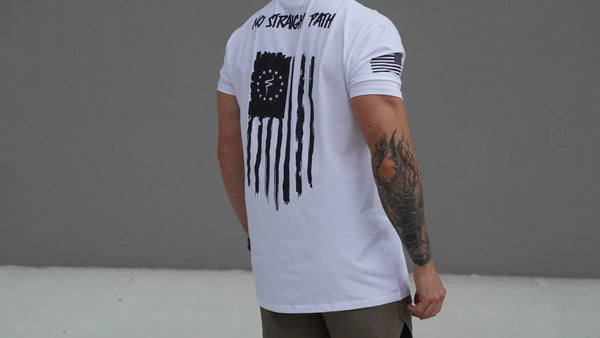 Person wearing a white t-shirt with a black flag design and text on the back, standing against a gray background.