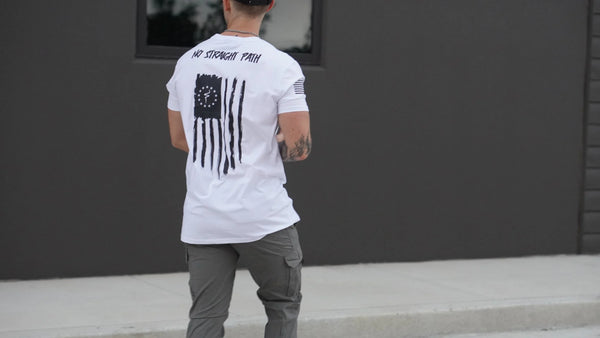 Person wearing a white t-shirt with a design on the back, standing against a dark wall.