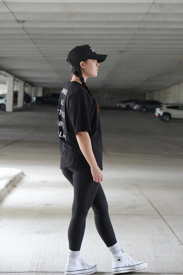 Person wearing a black outfit with white sneakers in an underground parking lot.