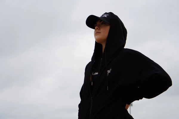 Person wearing a black hoodie and cap against a gray sky