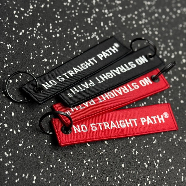 Three No Straight Path® keychains on a textured black background