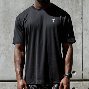 Person wearing a black t-shirt and shorts standing against a concrete wall.