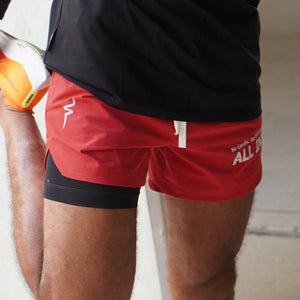 Red athletic shorts with white text worn by a person, against a neutral background.