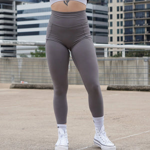Female wearing gray leggings and white sneakers on a rooftop with cityscape background