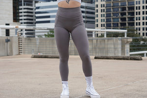 Female wearing gray leggings and white sneakers on a rooftop with cityscape background