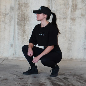 Girl in black outfit squatting against a textured wall.