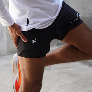 Person stretching with black athletic shorts and white shirt on a neutral background