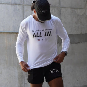 Person wearing a white long-sleeve shirt and black shorts with 'ALL IN.' text against a concrete wall.