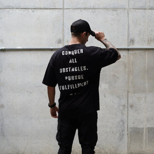 Person wearing a black t-shirt with motivational text against a concrete wall
