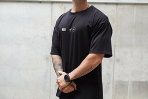 Person wearing a black t-shirt with a No Straight Path® logo against a light gray wall