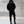 Person wearing a black hoodie and pants standing against a concrete wall.