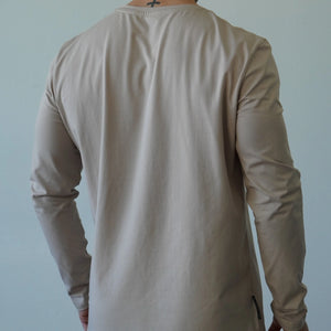 Person wearing a beige long-sleeve shirt against a plain background
