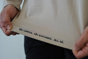 Person holding a beige pouch with motivational text 'No Limits. No Excuses. ALL IN.' on a plain background
