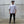 Man wearing a white t-shirt and black pants standing against a concrete wall.