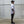 Person wearing a white t-shirt, black pants, and a cap standing against a concrete wall.