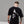 Person wearing a black t-shirt with a white skull graphic design on the back, standing against a gray background.