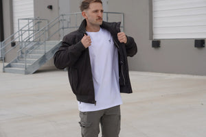Man wearing a black jacket, white t-shirt, and grey cargo pants in an outdoor setting.