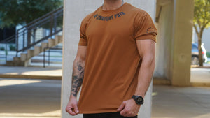 Man wearing a brown t-shirt with text, standing outdoors.