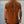 Person wearing a brown t-shirt with text and graphics on the back against a concrete wall.