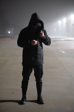 Person wearing a black hooded jacket and pants in a foggy outdoor setting