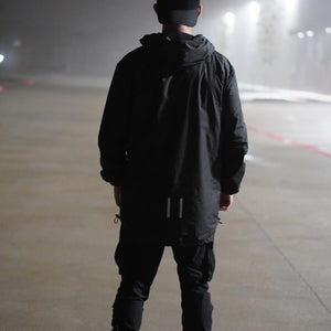 Person wearing a black jacket and pants standing on a foggy road at night.