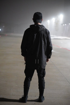 Person wearing a black jacket and pants standing on a foggy road at night.