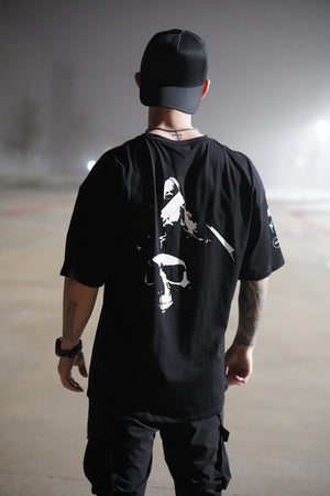 Person wearing a black t-shirt with a white  No Straight Path® skull graphic design, standing on a foggy road.