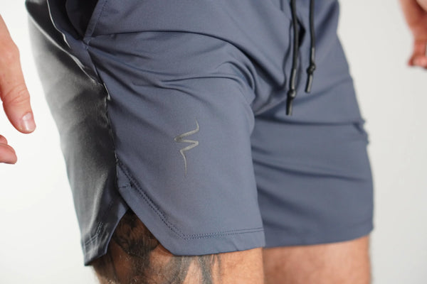 Close-up view of Gray-blue shorts with a No Straight Path® logo on the side pocket against a neutral background