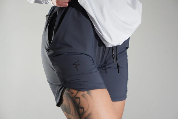 Person wearing dark blue shorts with a white shirt on a plain background